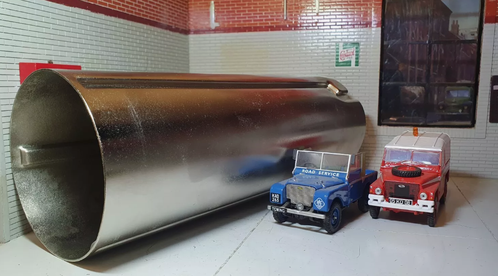 A side view of the filler neck repair part, cylindrical in shape, and an exterior view of the strengthening ridges. To the right are the blue and red model Land Rover Lightweights, used for illustration purposes.