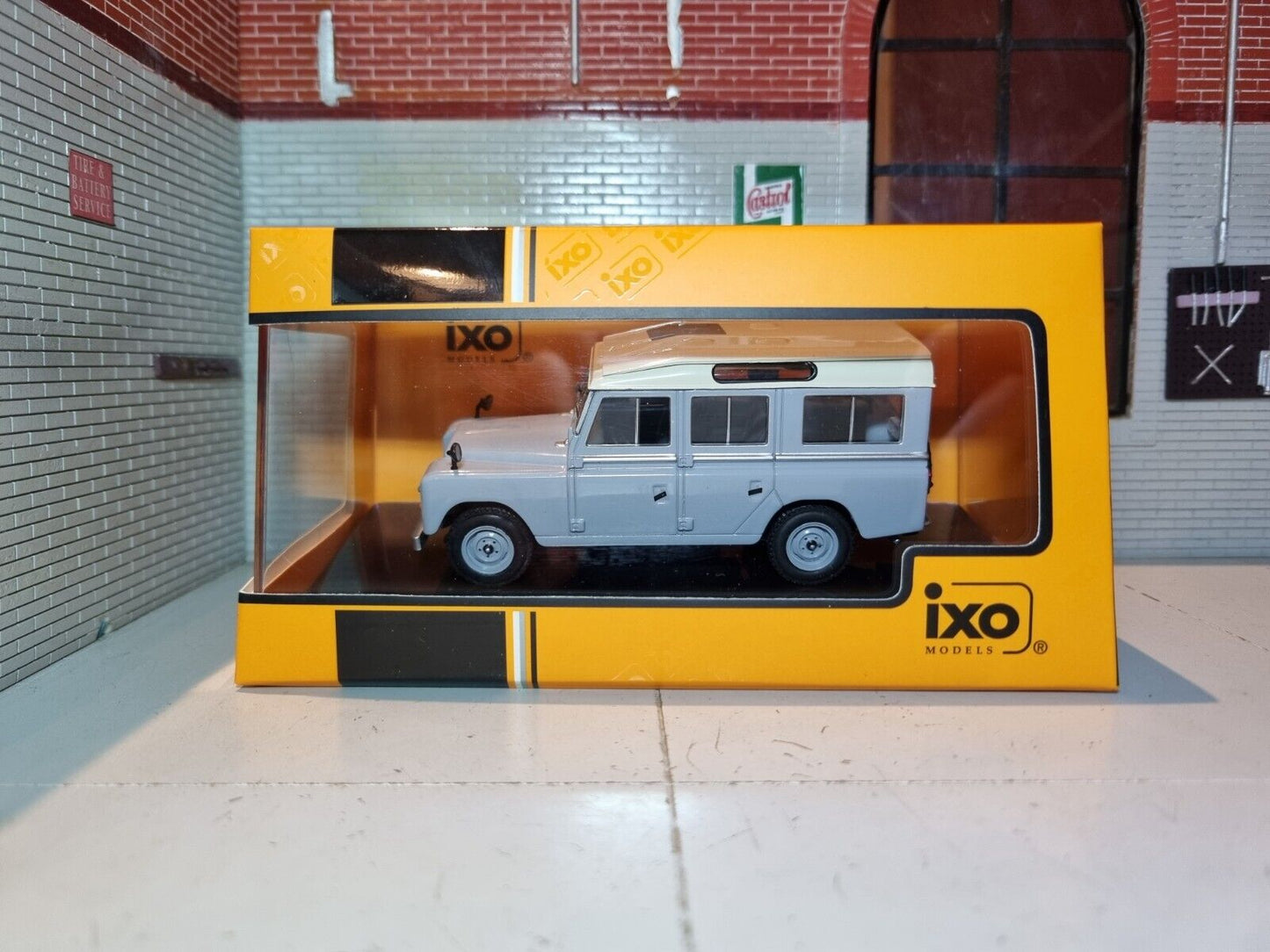 Boxed view of a model Land Rover Series 3 Station Wagon in light blue with an off-white roof. a logo for ixo models is in the bottom right corner.