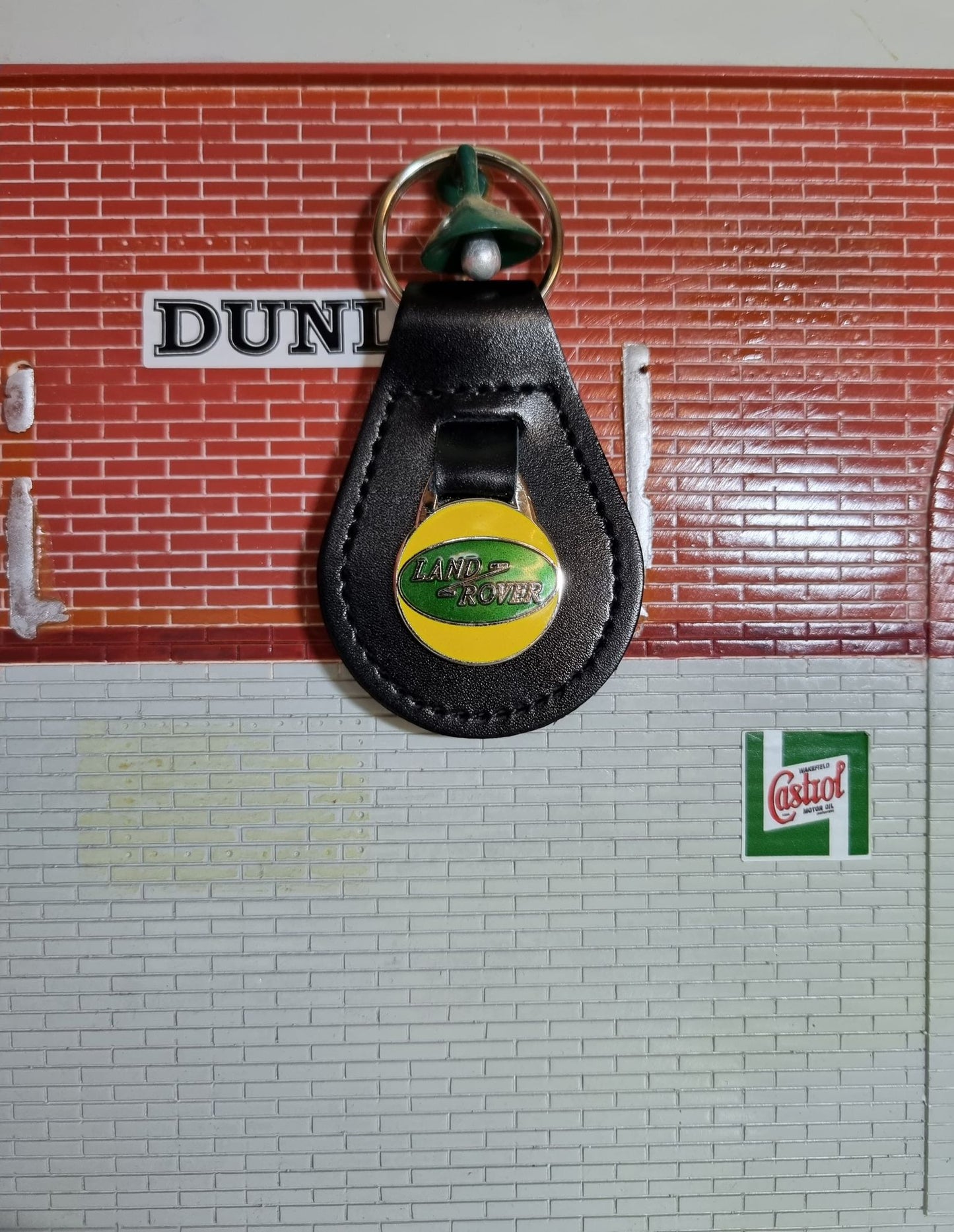 A Land Rover Key ring. The classic Green oval logo is set into a yellow background, attached to a black leather fob.