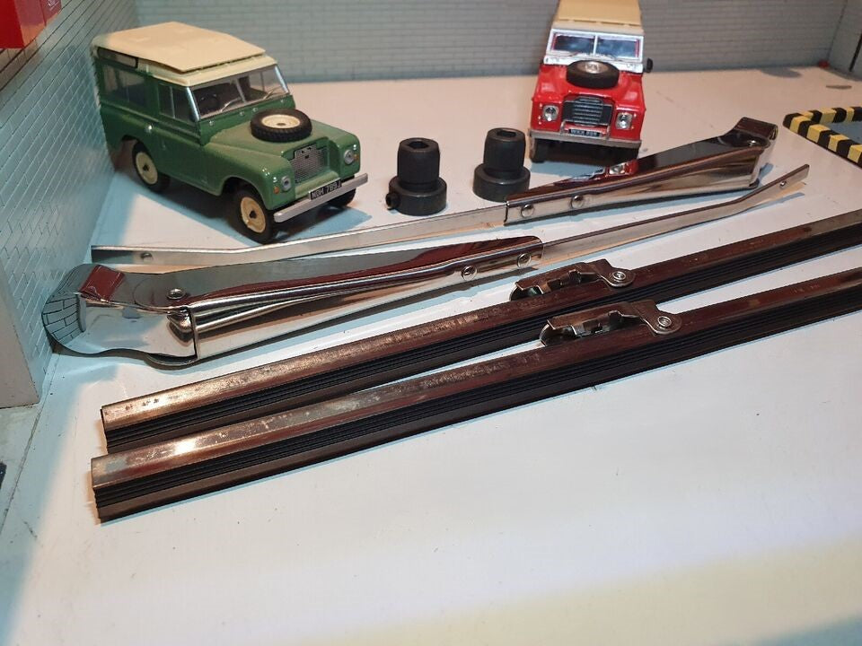 Wiper Blades and Wiper Arms in Stainless Steel and Spindle Adapters Kit. Behind are a Green (left) and Red (right) model Land Rover for Illustration Purposes.