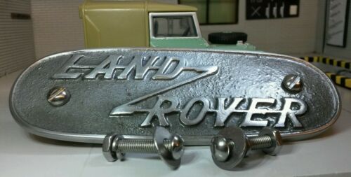 Aluminium variant of a pressed aluminium Land Rover Series 1 grill badge, behind is a model Land Rover Series (for illustration purposes only. In front of the badge are domed headed slot machine screws for fitting.