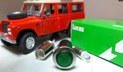 Green LED dash panel warning light with chrome bezel, in the background is a miniature red Land Rover toy vehicle for display purposes and a box labelled 'Lucas'.