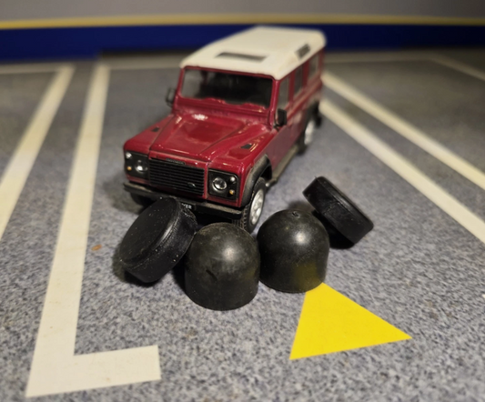 Four black round rubber buffers are scattered in front of a toy land rover.