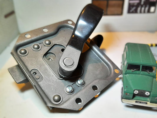 Metal lever mechanism on a white surface with a toy car in the background