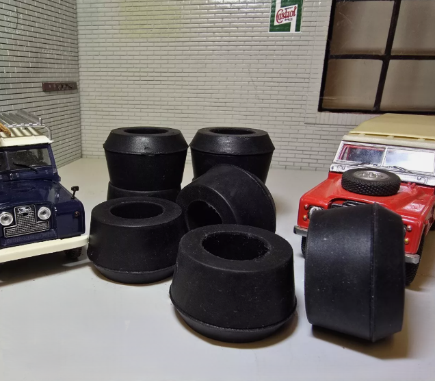 A selection of Suspension bushes on a grey surface, to the left and right are blue and red Land Rover models for illustrative purposes.