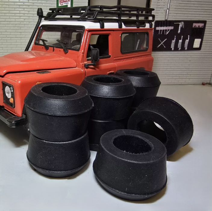 A selection of Suspension bushes on a grey surface, behind is a red Land Rover Defender model for illustrative purposes.