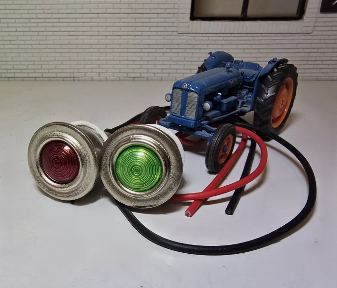 Red and Green Warning Lights with side by side with silver bezels and wiring tails. In the background is a Fordson Tractor for illustration purposes.