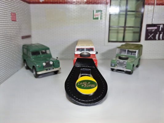 A Land Rover Key ring. The classic Green oval logo is set into a yellow background, attached to a black leather fob.