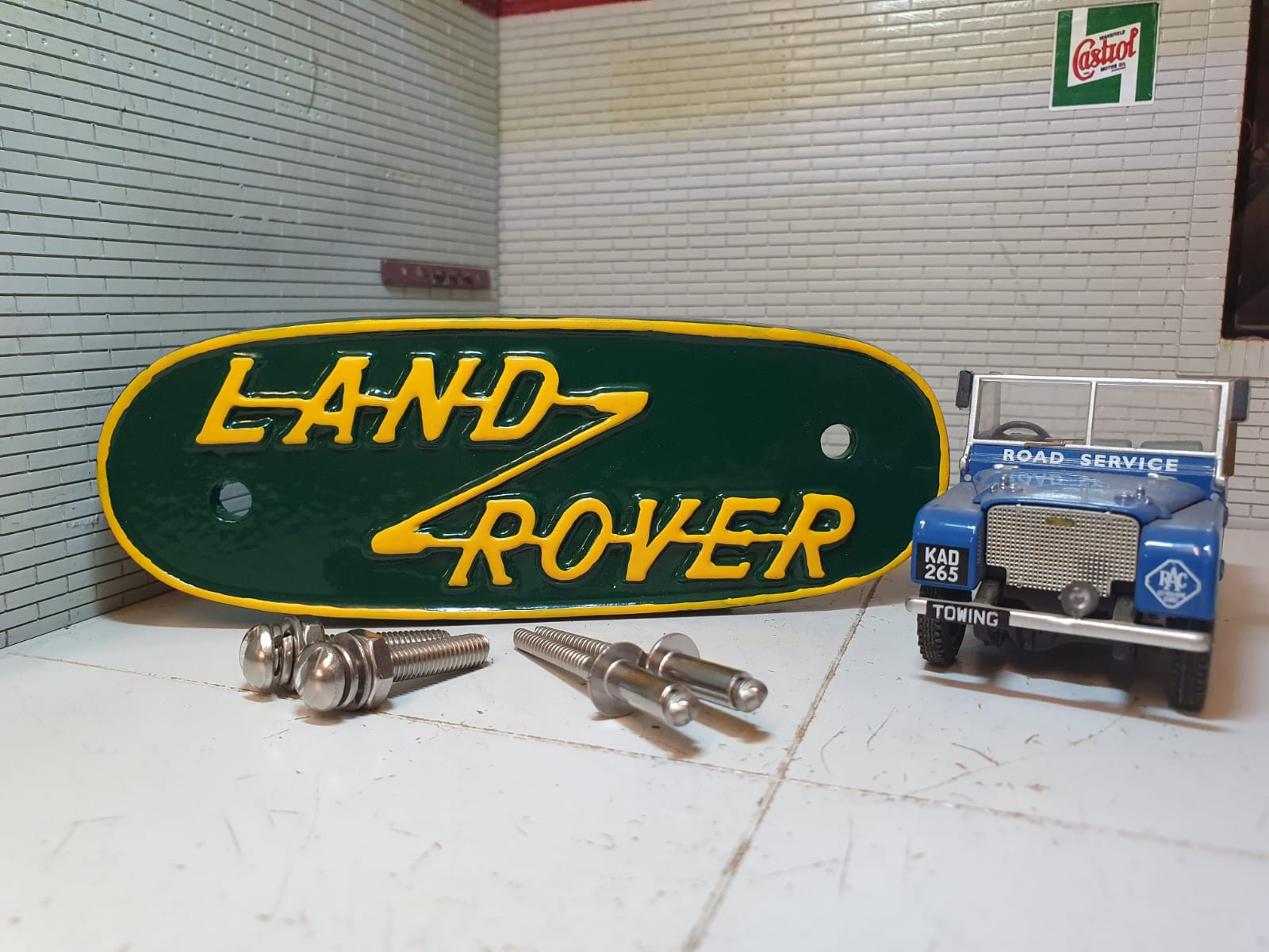 Yellow and green variant of a pressed aluminium Land Rover Series 1 grill badge, on the right is the model Series 1 (for illustration purposes only.) In front of the badge are stainless rivets and domed headed slot machine screws for fitting.