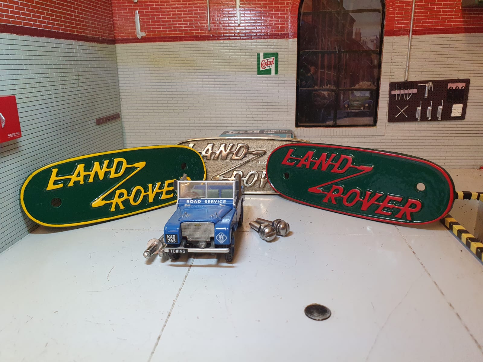 Land Rover 1948 to 1952 Cast Aluminium Grill/Tub Badges Yellow and green on the left, Brass in the middle, red and green on the right with fixings and a Model of a Series 1 Land Rover in front (model for illustration purposes only)