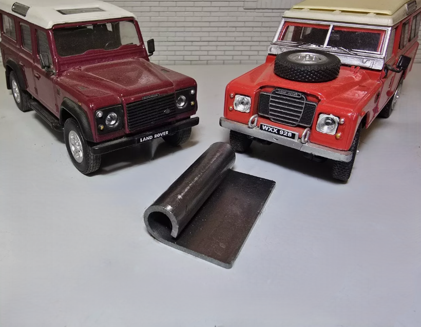 Bulkhead Air Vent Flap Hinge Bracket in the foreground laid down. To the left and right are Red Land Rover Defender and Series Models for Illustration Purposes.