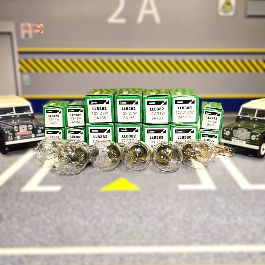Collection of car bulbs and boxes on a gray surface with vehicle models in the background.