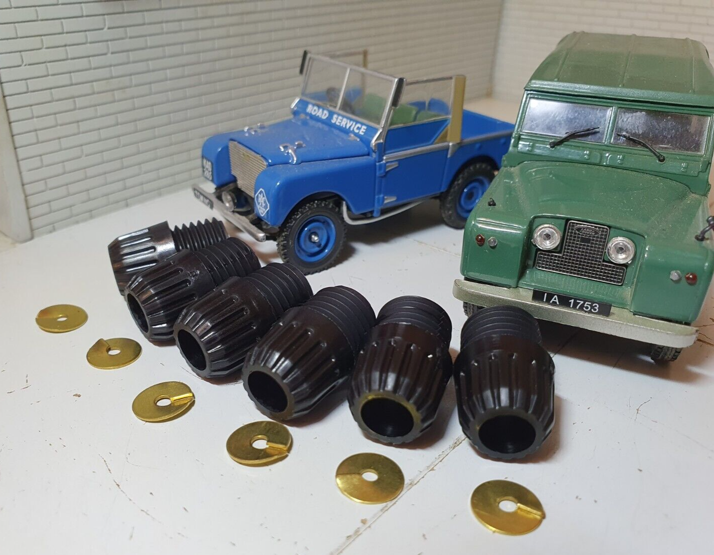 Six Lucas Acorn Spark Plug Screw Caps With Metal Washers And Two Model Land Rovers In The Background